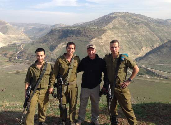 Three IDF soldiers standing with civilian against a mountainous backdrop
